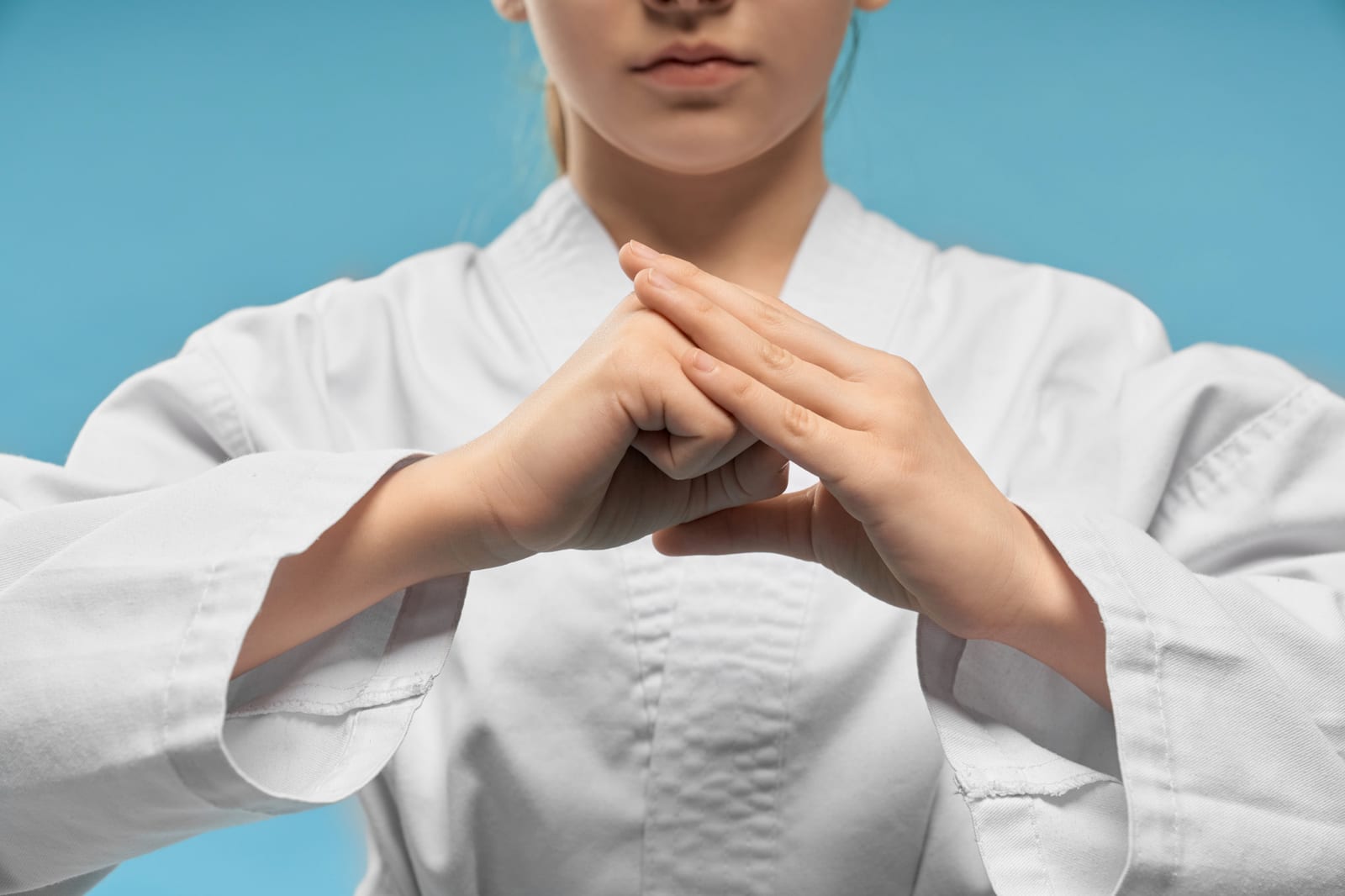 Close-up of a martial artist in a white dobok forming a covered-fist salute against a blue background