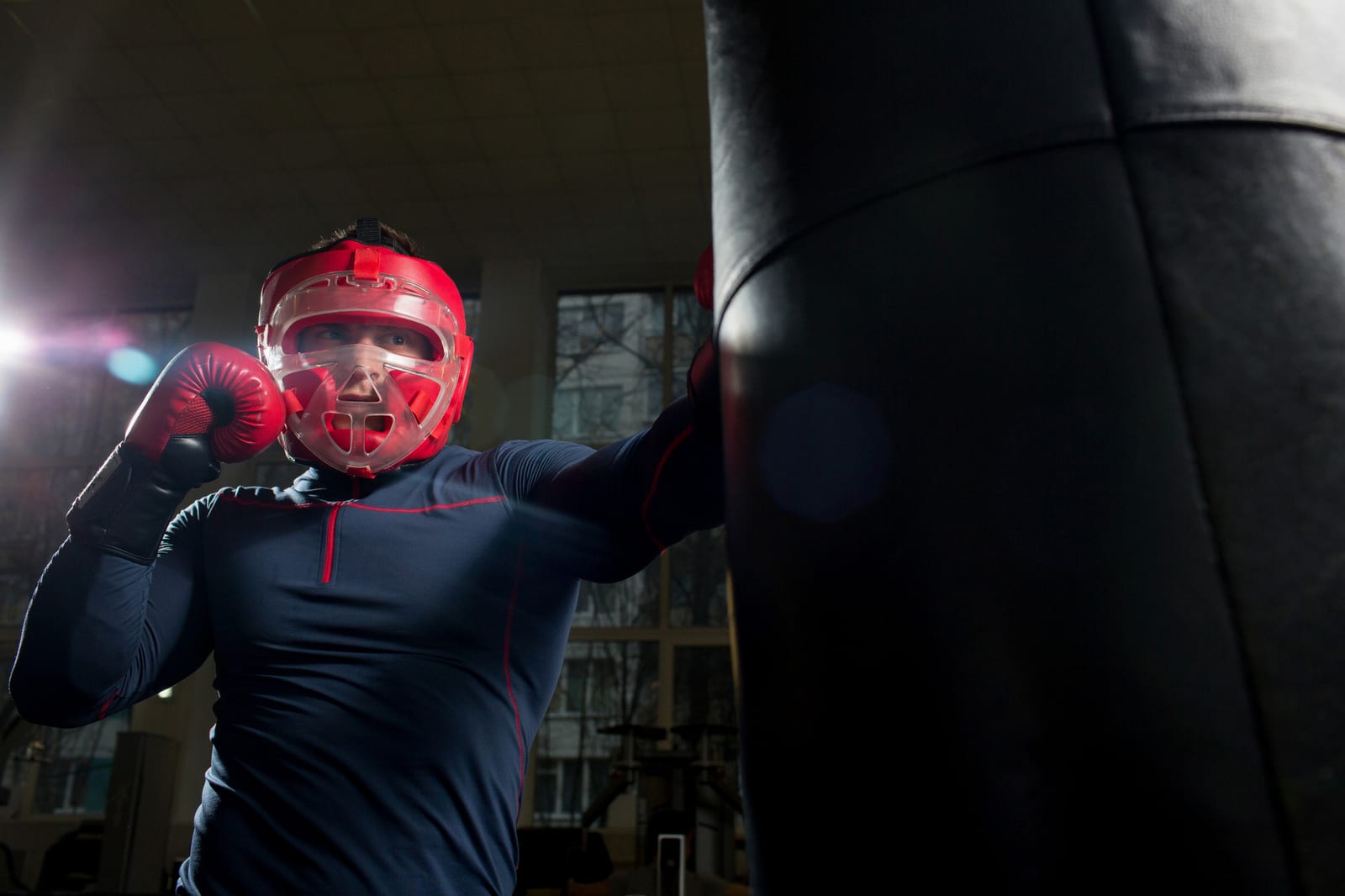 A man in red headgear and red gloves holding his guard beside a heavy bag