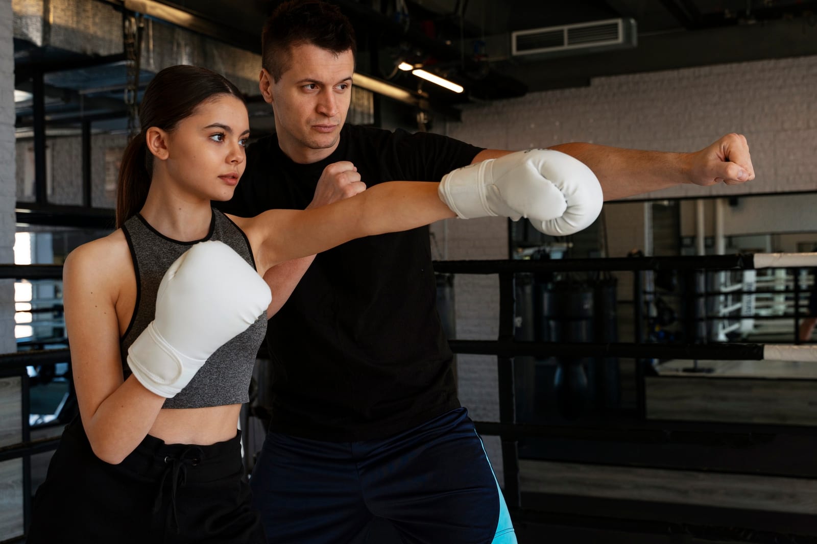 A male trainer guiding a woman's gloved straight punch during a self-defense lesson