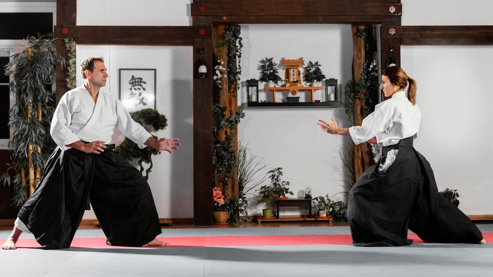 Two aikido practitioners in hakama squaring off on a red mat in a traditional dojo